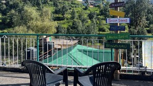 A terrace with a view of mountains, a signpost with directions, and a railing. - Cozy Mountain-View Room near Mcleodganj in Dharamshala Homestay (Dharamshala)