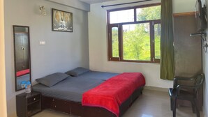 A bedroom with a bed, a ceiling fan, a window with curtains, a chair, and a wall-mounted TV. - Cozy Mountain-View Room near Mcleodganj in Dharamshala Homestay (Dharamshala)