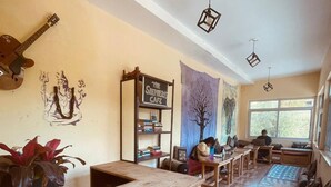 A cozy cafe with wooden furniture, a guitar on the wall, and a large window. - Cozy Mountain-View Room near Mcleodganj in Dharamshala Homestay (Dharamshala)