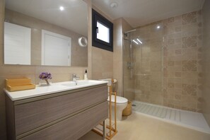 A modern bathroom with a large mirror, a wooden vanity, a toilet, and a glass-enclosed shower.