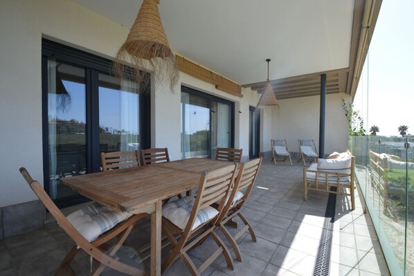 A spacious balcony with a wooden table and chairs, large windows, and a view of the landscape.