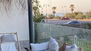 A balcony with a wicker chair and cushions, overlooking a road with cars and palm trees. - Los Flamencos 4004 - Two Bedroom Apartment, Sleeps 5 (Punta del moral)