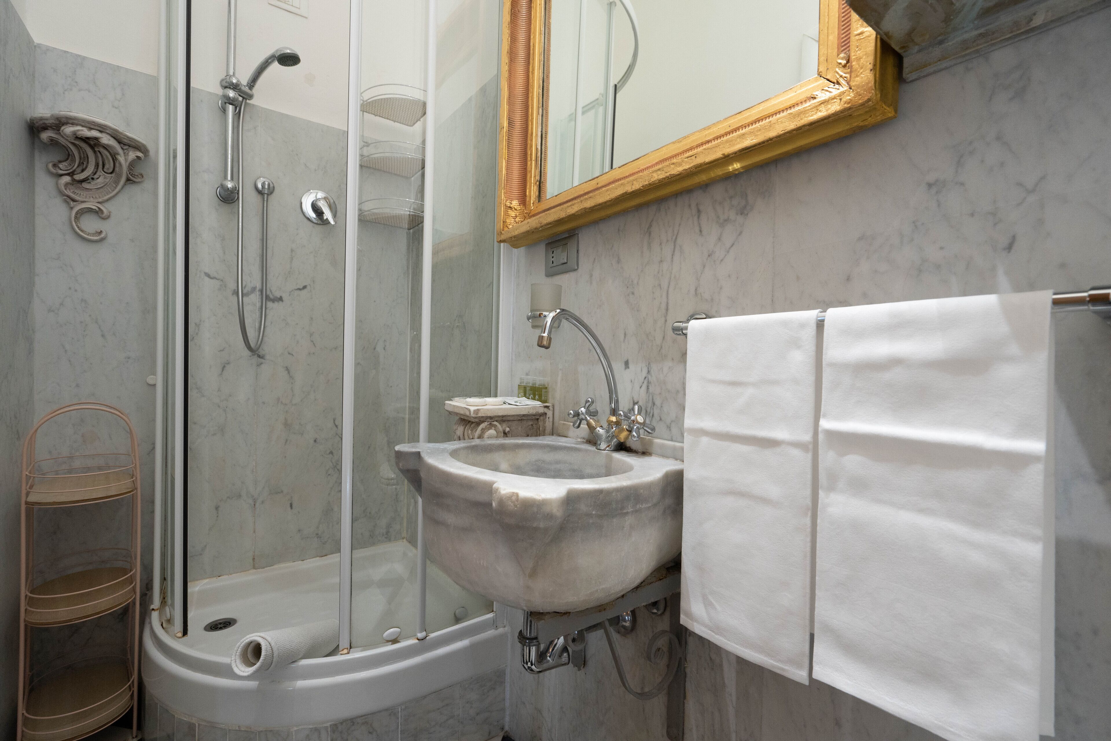 Une salle de bain avec un lavabo en marbre, une cabine de douche en verre, une serviette blanche et un miroir avec un cadre doré.