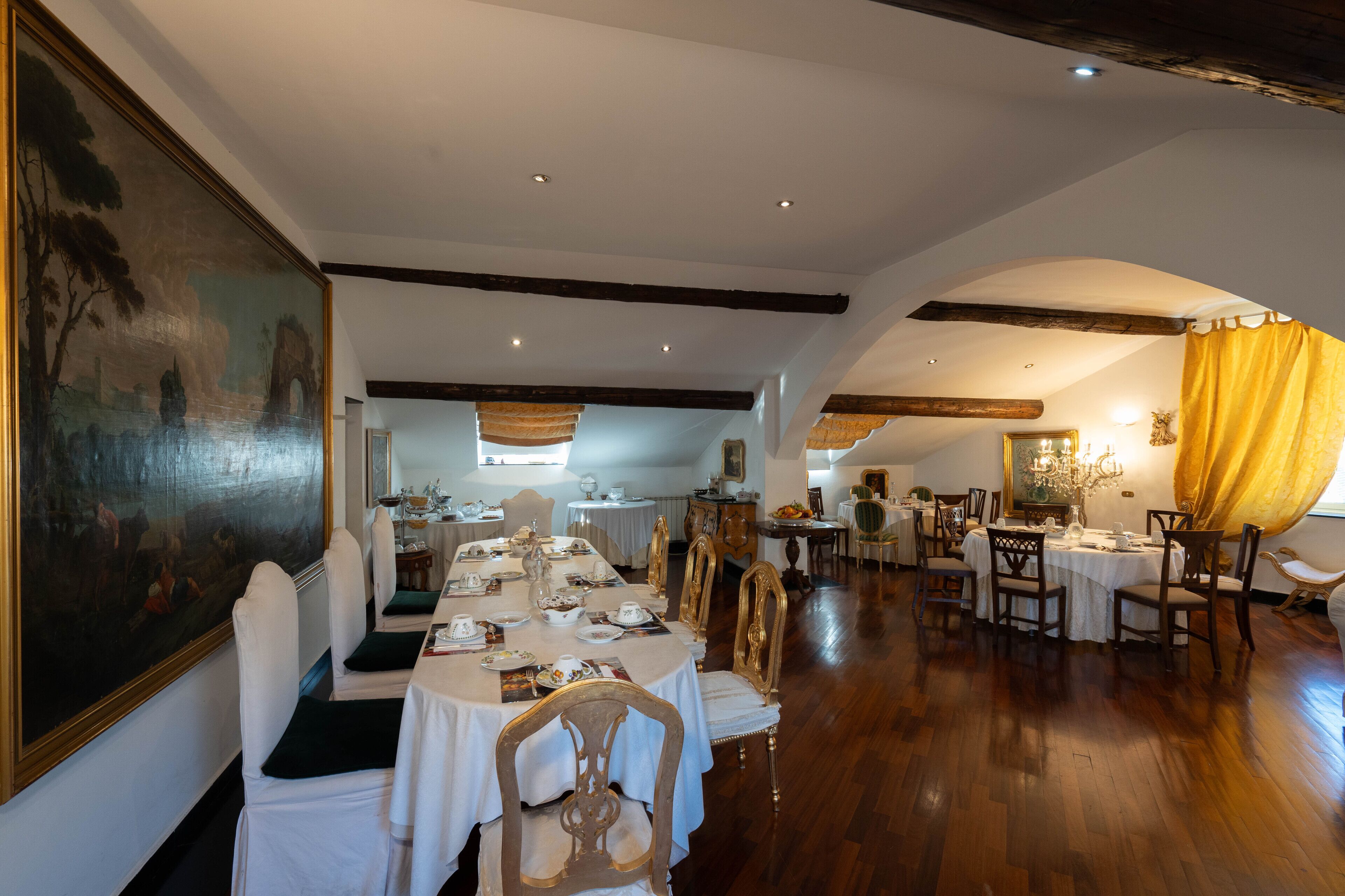 A dining area with multiple tables set for a meal, wooden floors, and a large painting on the wall.