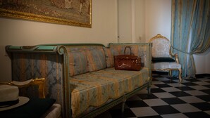 A room with a checkered floor, a patterned sofa, a chair with a decorative backrest, and a large framed painting on the wall. - San Giorgio Rooms (Genoa)