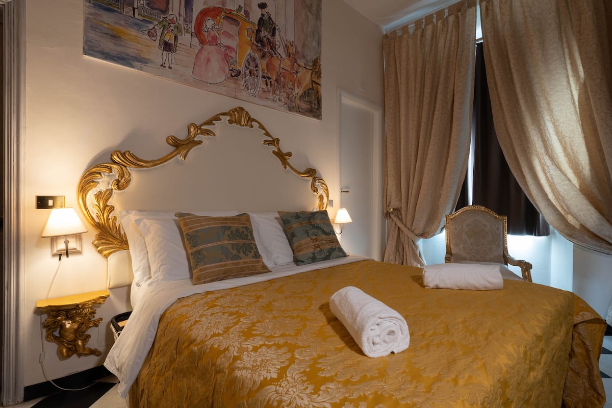 A hotel room with a large bed, ornate headboard, and a painting above the bed.