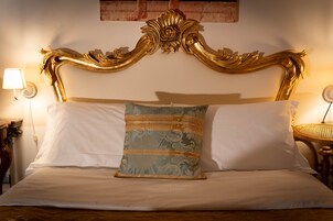 Una cama con cabecera dorada, almohadas blancas y un cojín decorativo.