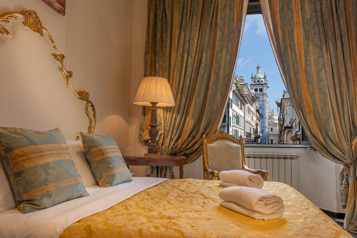 A hotel room with a bed, a lamp, a chair, and a view of a cityscape through curtains.