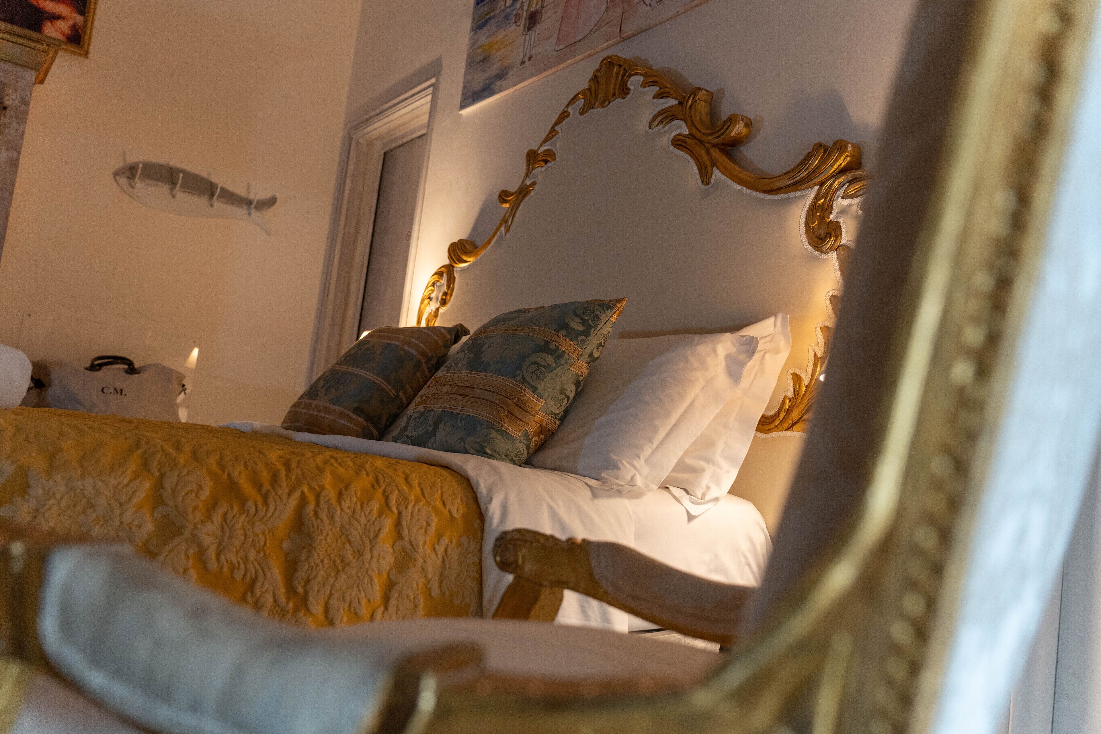 A bed with ornate headboard, multiple pillows, and a decorative wall hanging.