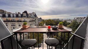 A balcony with two wicker chairs, a wooden table, two potted plants, a red mug, and a teapot. - Le Marais, rue de Bretagne Square du Temple - Elie Wiesel (Paris)