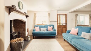 A cozy living room with a fireplace, blue sofas, and a wooden floor. - Tastefully furnished spacious cottage - perfect for family gatherings! (Buckland Newton)