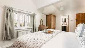 A bedroom with a large bed, a wooden wardrobe, a dresser, a mirror, and a window with curtains. - Tastefully furnished spacious cottage - perfect for family gatherings! (Buckland Newton)