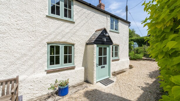 A white building with green trim and a small porch. - Tastefully furnished spacious cottage - perfect for family gatherings! (Buckland Newton)