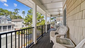 A covered porch with wicker chairs, a ceiling fan, and a view of neighboring houses and trees. - 7BR Pet-Friendly Home w/ EV Charger & Room for 18+ Guests (Bethany Beach)