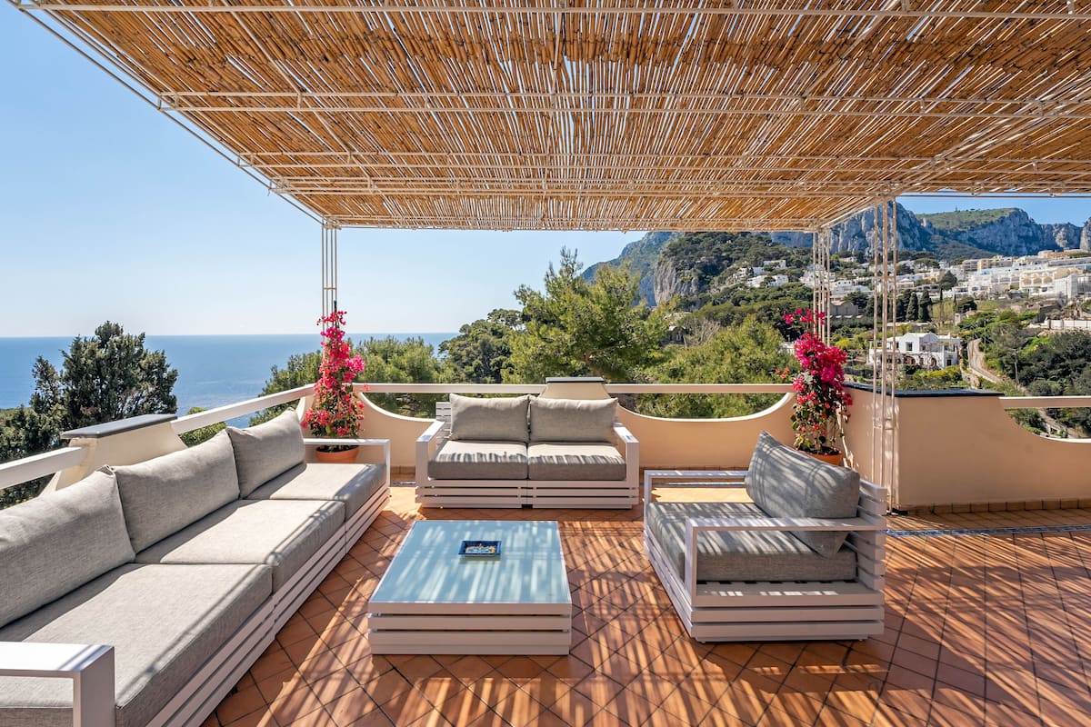 A terrace with a wooden pergola, a sofa set, a coffee table, and potted plants.