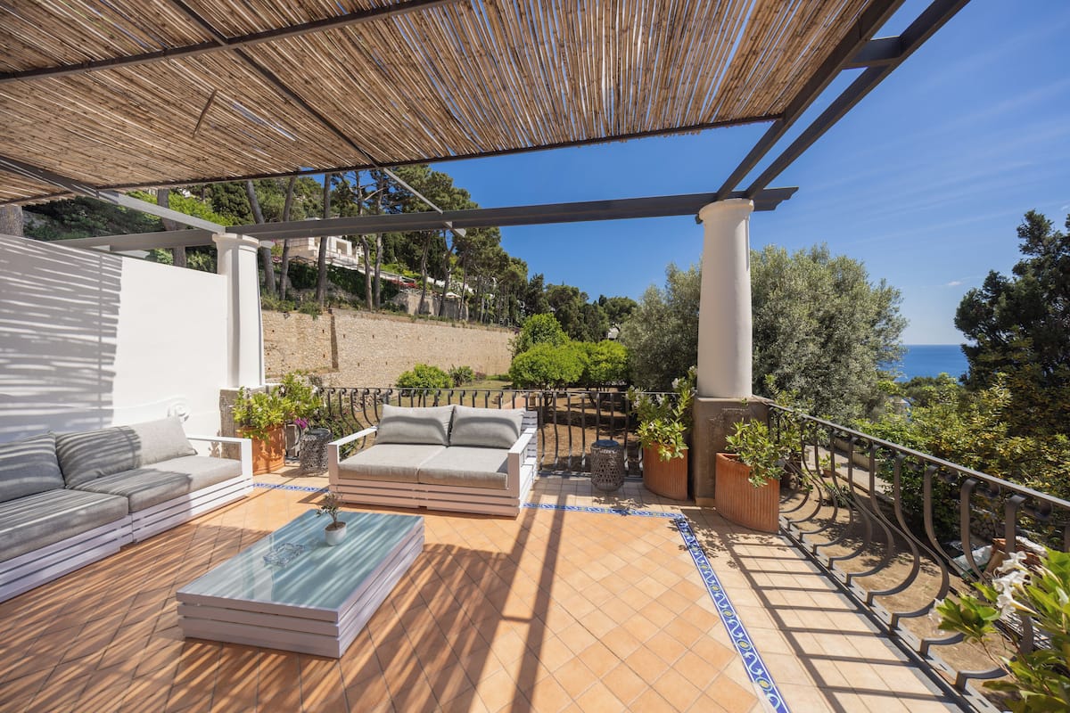 A terrace with a sofa, a glass coffee table, and potted plants.