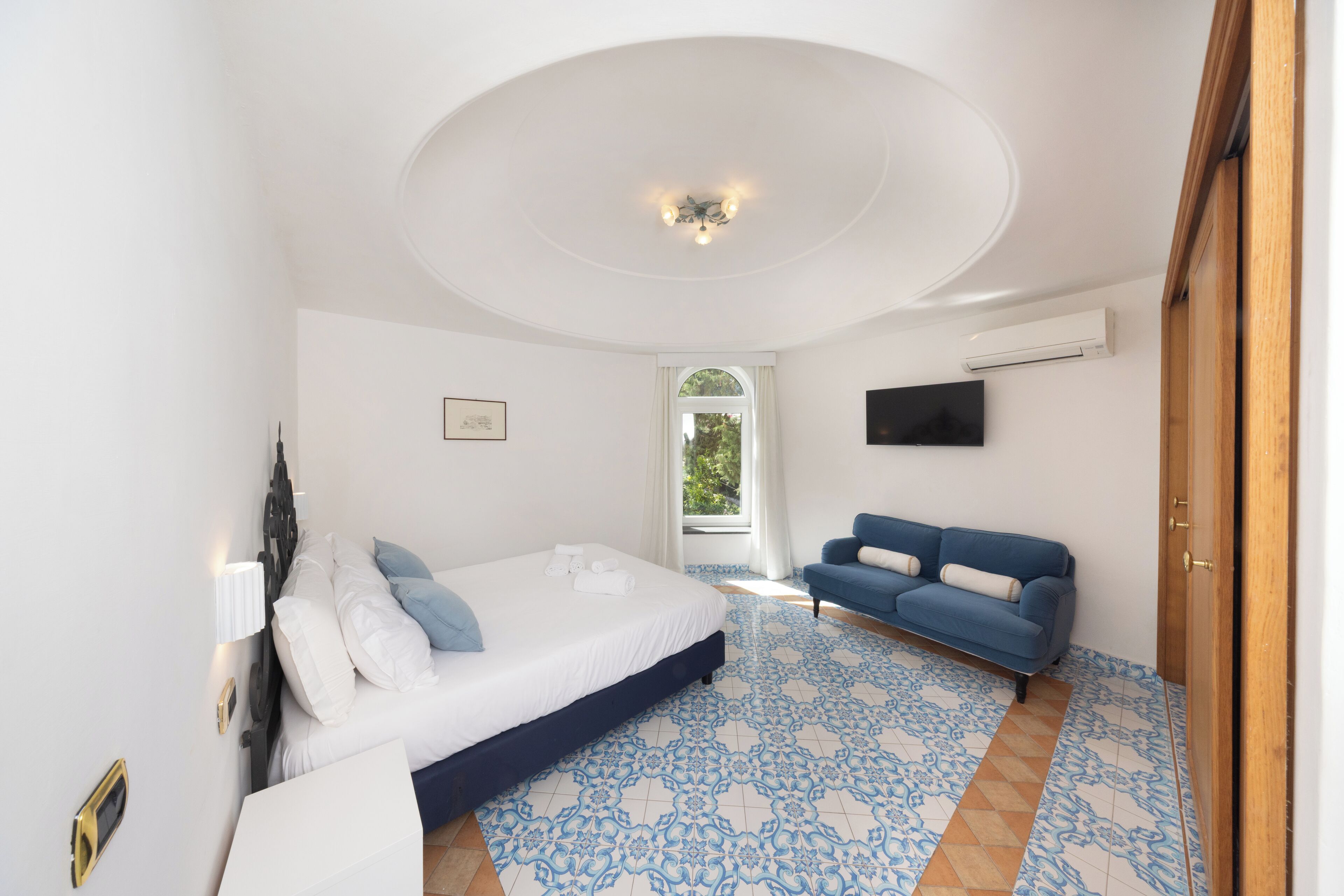 A bedroom with a bed, a blue sofa, a TV, and a window.