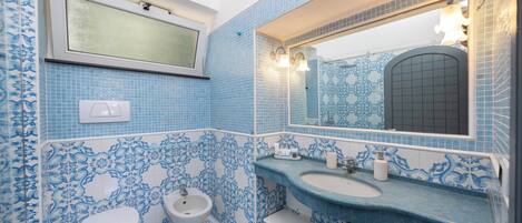 A bathroom with blue patterned tiles, a white toilet, a bidet, and a sink with a mirror above it.