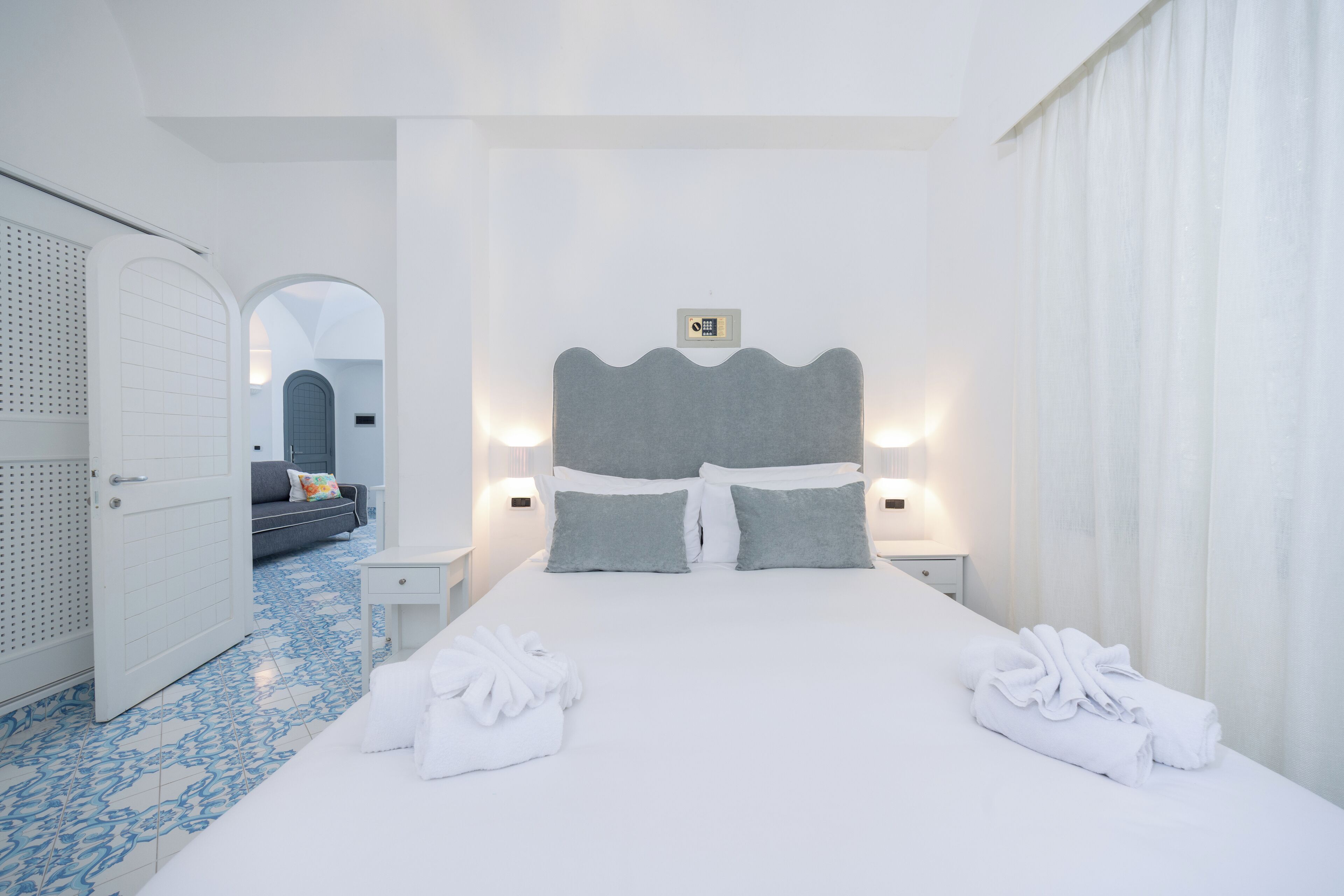 Une chambre d’hôtel avec un grand lit, deux tables de chevet, une commode, une salle de bain avec douche et un petit coin salon comprenant un canapé et une table basse.