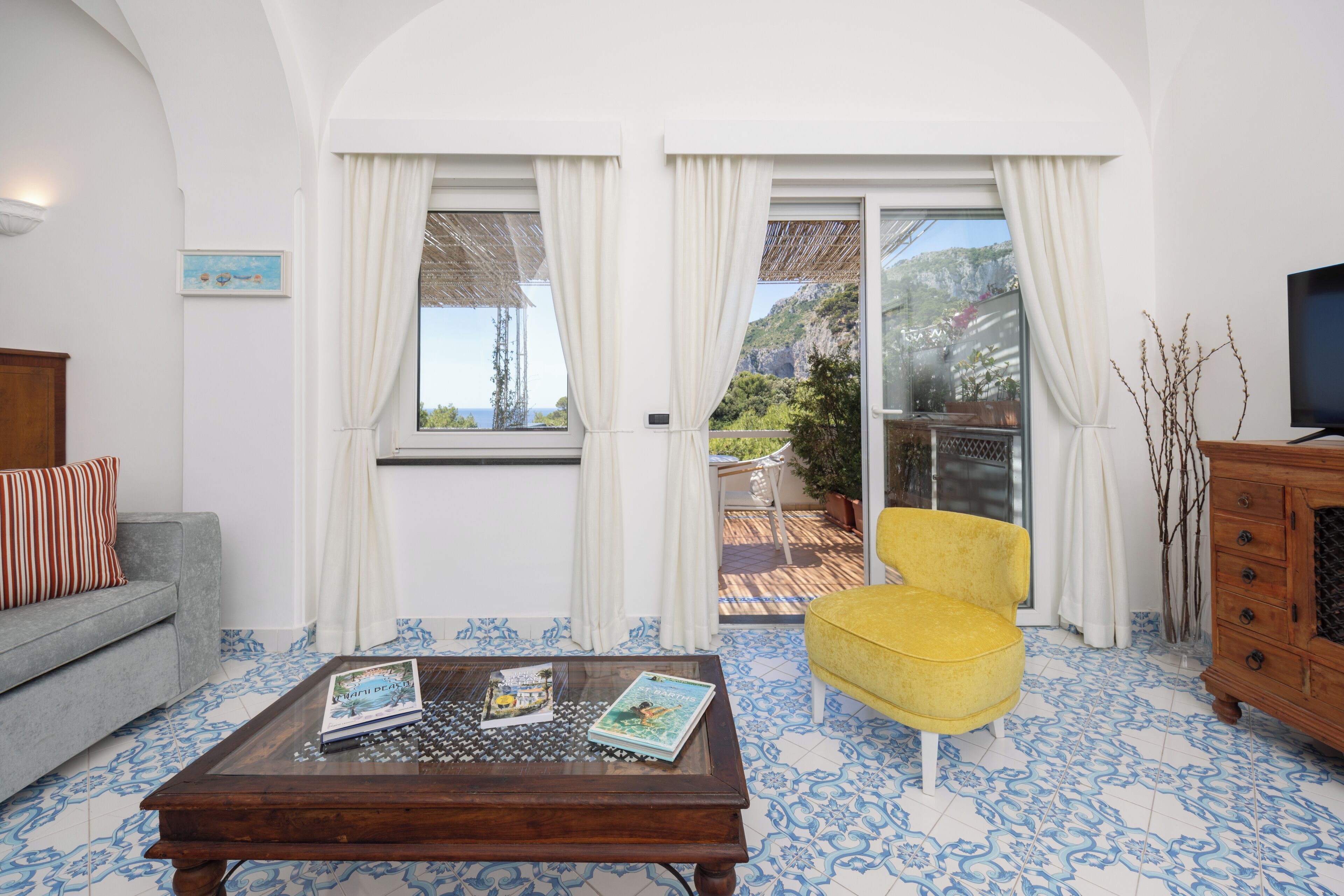 A living room with a sofa, a yellow chair, a coffee table with books, and a TV.