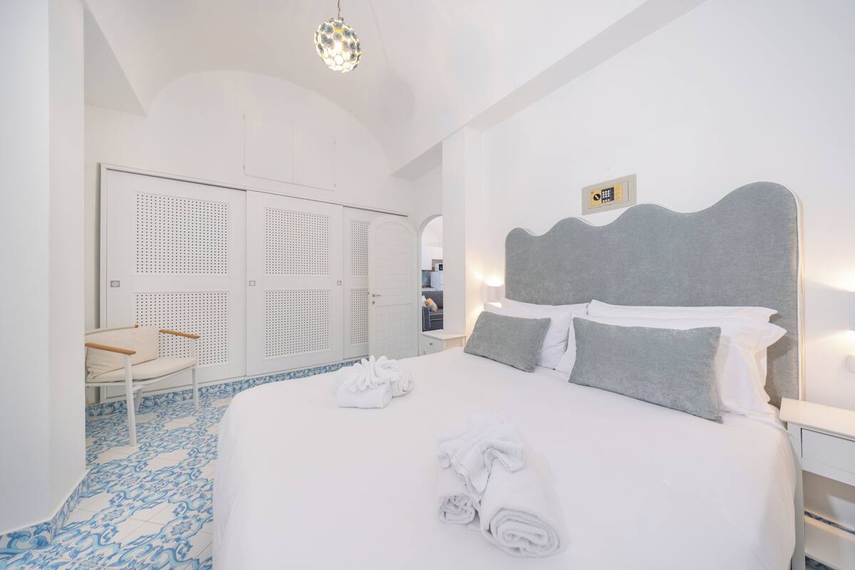 A hotel room with a large bed, a chair, a wardrobe, and a bathroom.