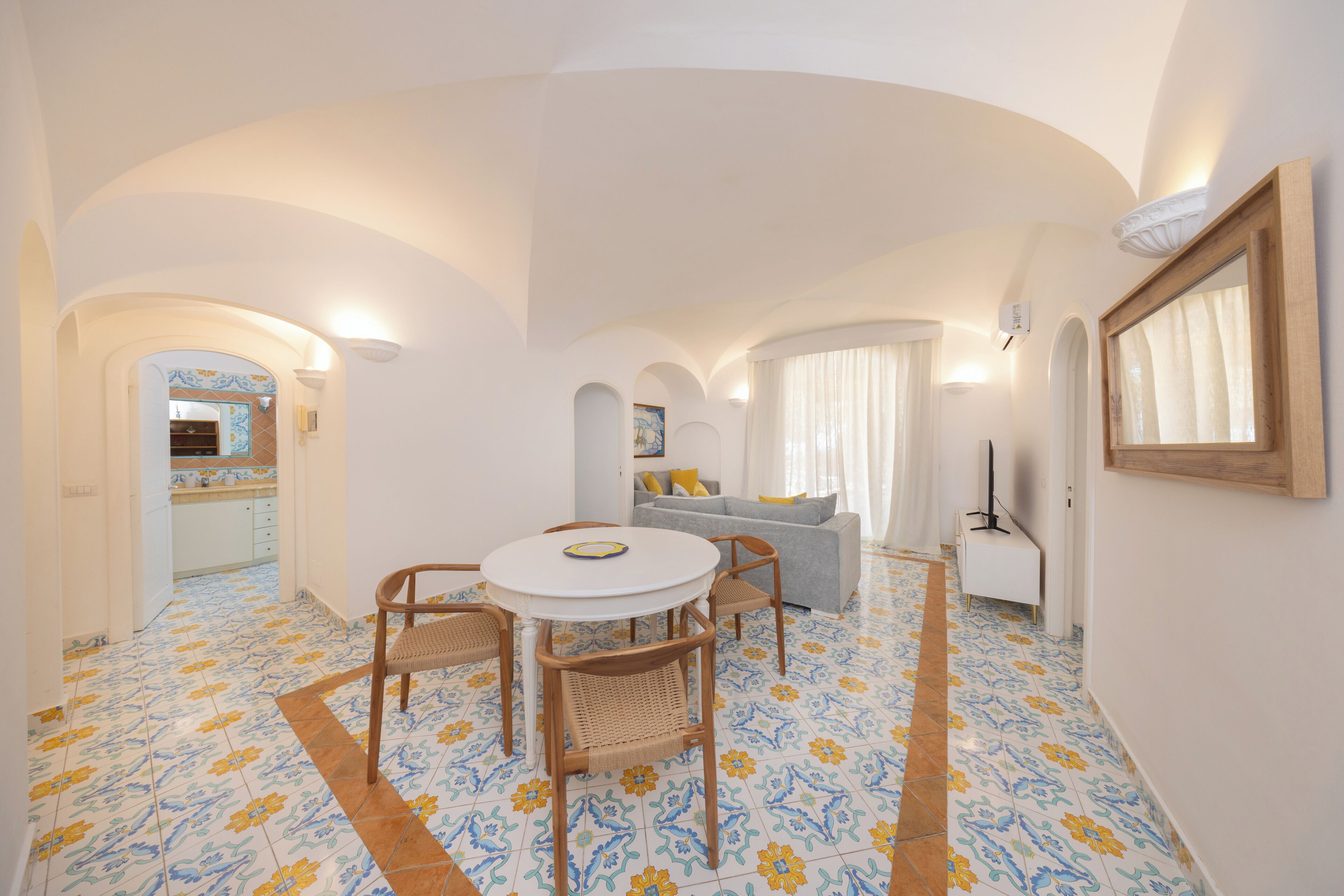 A room with a round table and chairs, a sofa, and a mirror on the wall.