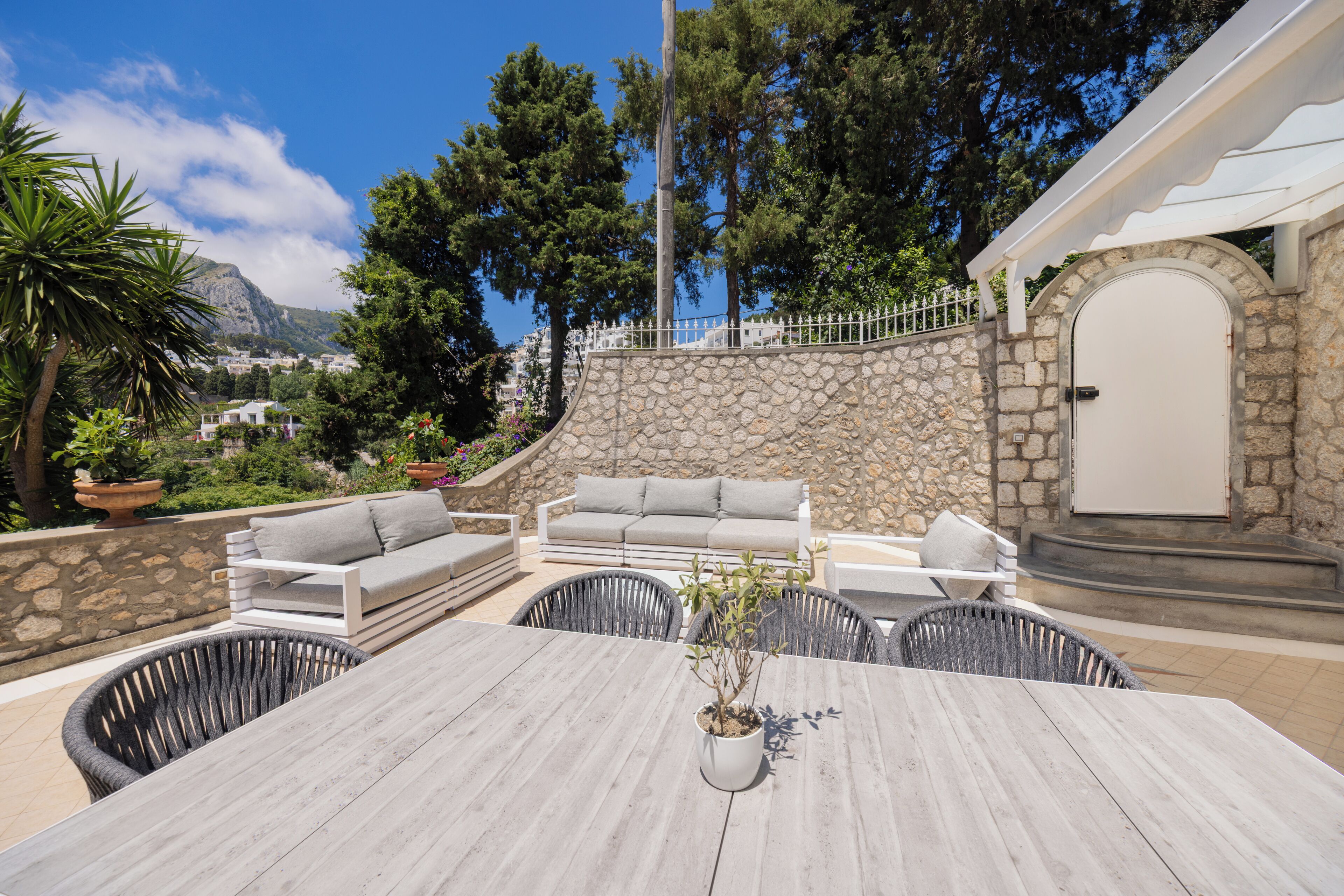 An outdoor patio with a stone wall, a white door, and a grey sofa.