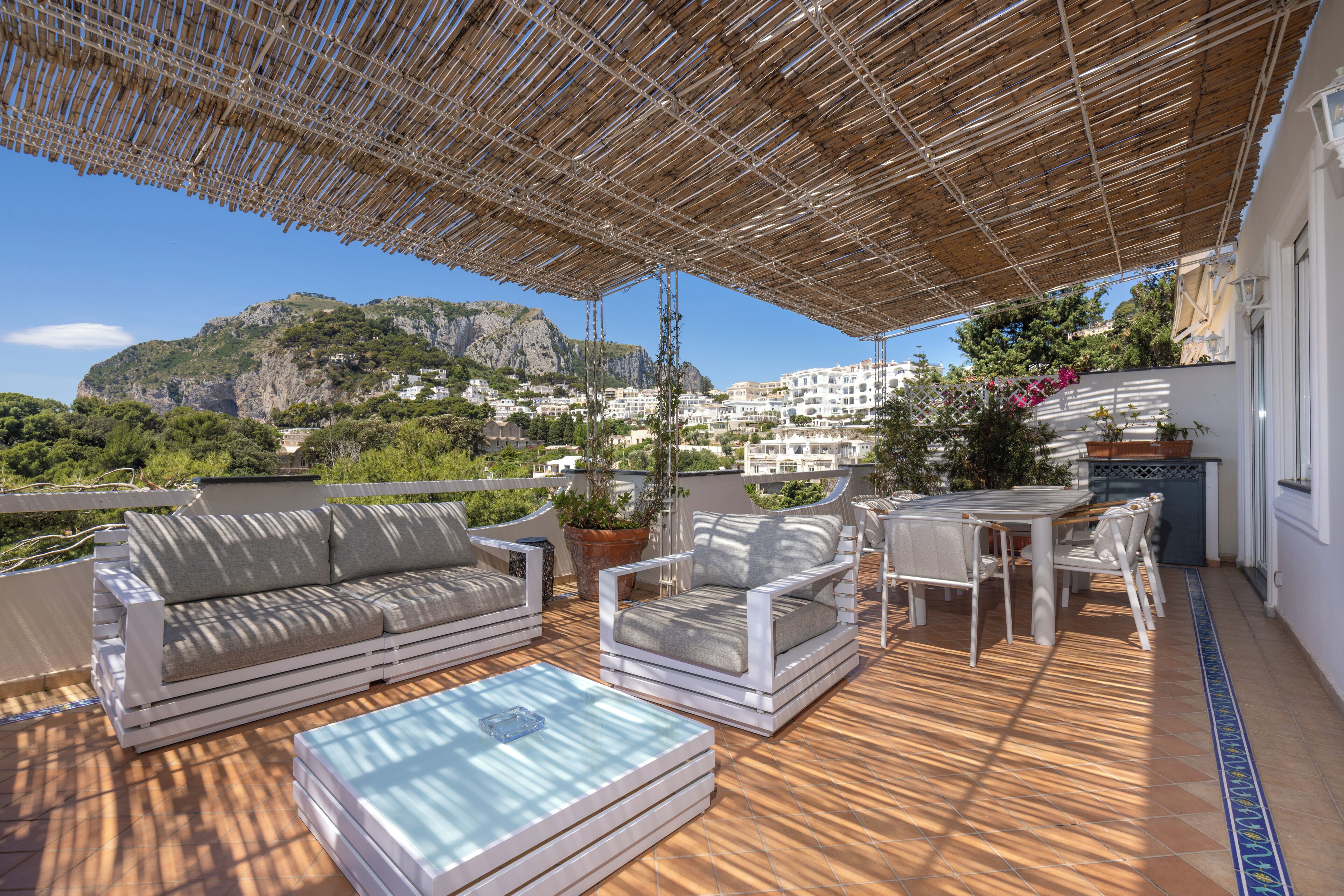 An outdoor patio with a wooden deck, white furniture, and a view of a mountainous landscape.