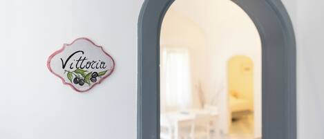 Una puerta que da a una habitación con pared blanca y un letrero que dice "Vittoria" con un diseño decorativo.