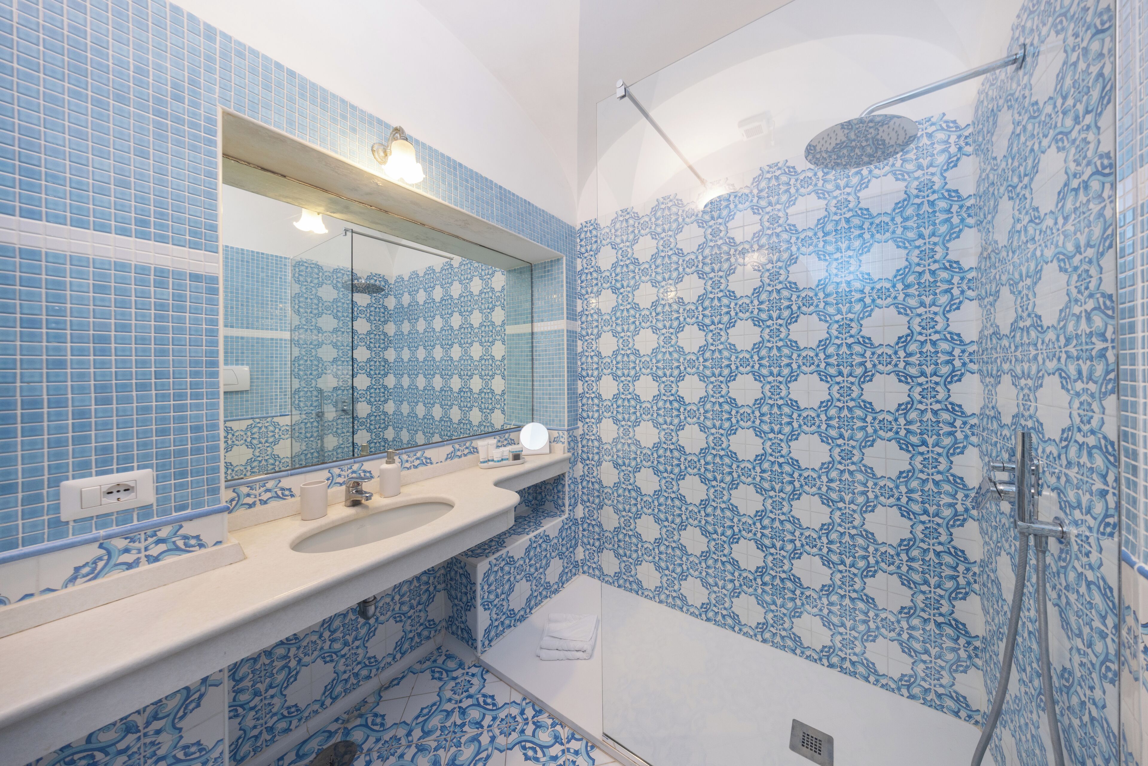 Un baño con azulejos azules estampados, un lavamanos, un espejo y una ducha.