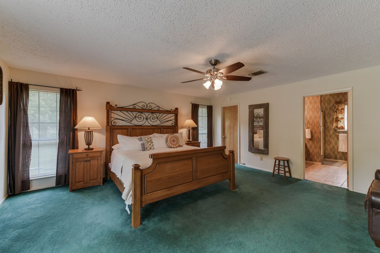 A bedroom with a wooden bed, two bedside tables with lamps, a ceiling fan, and a view of the bathroom through an open door.