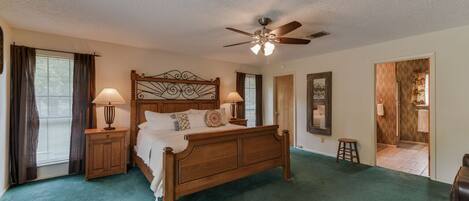 A bedroom with a wooden bed, two bedside tables with lamps, a ceiling fan, and a view of the bathroom through an open door.