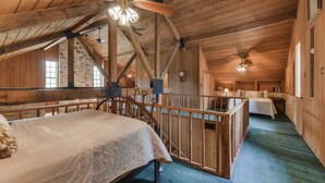 Ein gemütliches Schlafzimmer im Dachgeschoss mit Holzbalkendecke, einem Bett, einem Schreibtisch und einer Treppe.