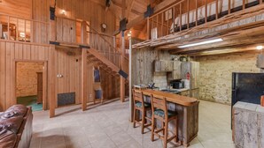 Ein rustikales Blockhaus-Interieur mit einer Holztreppe, einer Essecke mit Barhocker, einer Küche mit Steinwänden und einem Schlafbereich auf dem Dachboden.