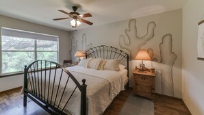 A bedroom with a bed, a ceiling fan, a nightstand, and a window with a view of trees.