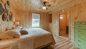 A wooden-paneled bedroom with a bed, a ceiling fan, a window, and a green dresser.