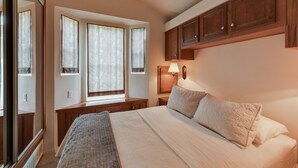 Ein Schlafzimmer mit einem großen Bett, einem Nachttisch, einer Lampe und einem Fenster mit Vorhängen.