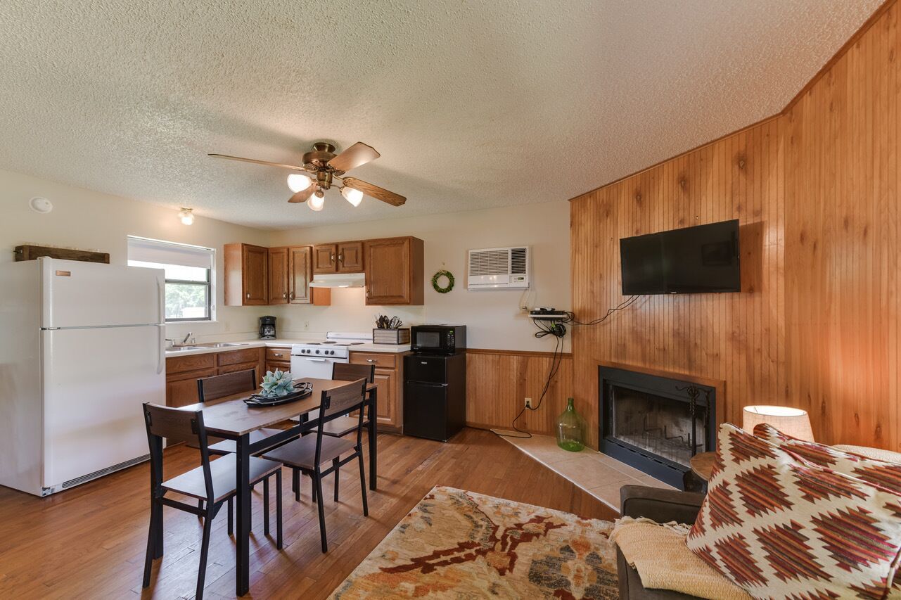 A compact kitchen with wooden cabinets, a refrigerator, stove, microwave, and a fireplace.