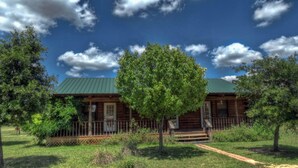 A log cabin with a green roof, surrounded by trees and a grassy yard.