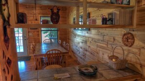 A wooden cabin interior with a dining area, wooden walls, and a window.