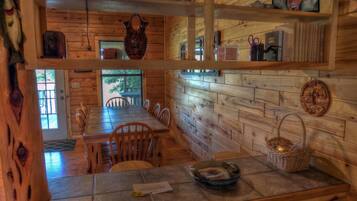 A wooden cabin interior with a dining area, wooden walls, and a window.