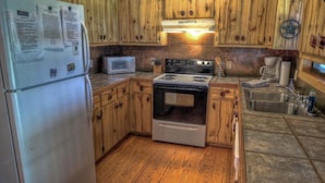 A kitchen with wooden cabinets, a stainless steel refrigerator, a microwave, a stove, and a sink.