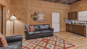 Un espacio habitable pequeño con interior de madera, un sofá de cuero, una zona de cocina y una alfombra estampada.