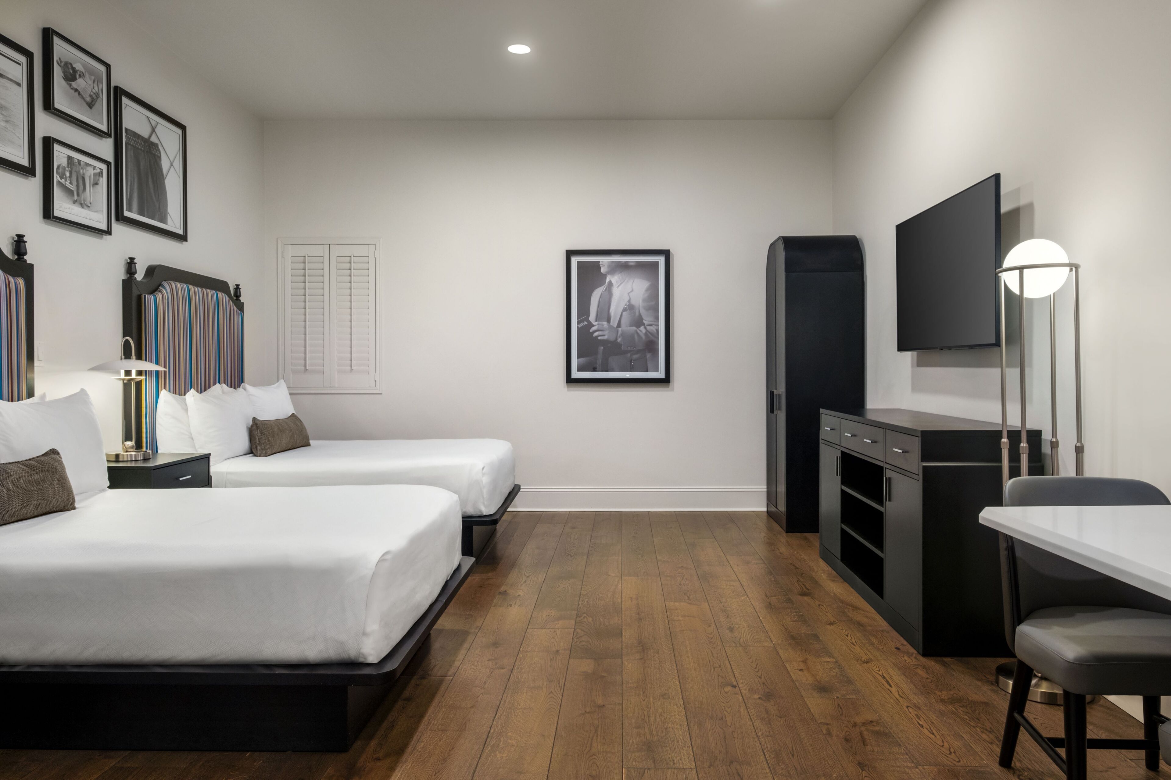 A hotel room with two beds, a desk, a TV, and a bookshelf.