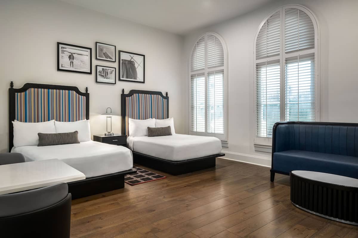 Ein Hotelzimmer mit zwei Betten, einem blauen Sofa, einem kleinen Tisch und einem Fenster mit Jalousien.