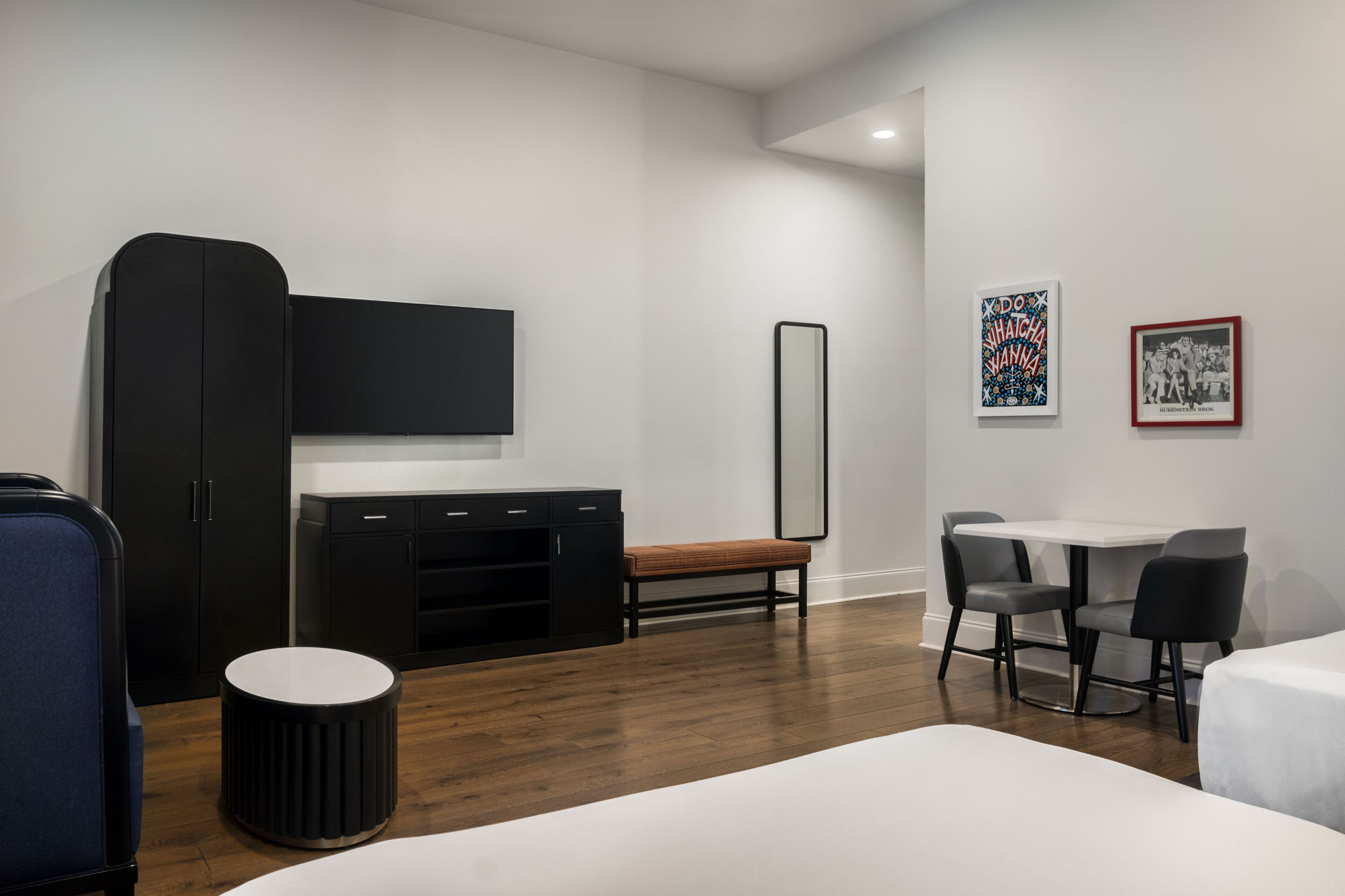A modern hotel room with a bed, a desk, a chair, a TV, a wardrobe, and artwork on the wall.