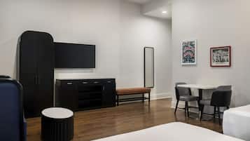 A modern hotel room with a bed, a desk, a chair, a TV, a wardrobe, and artwork on the wall.