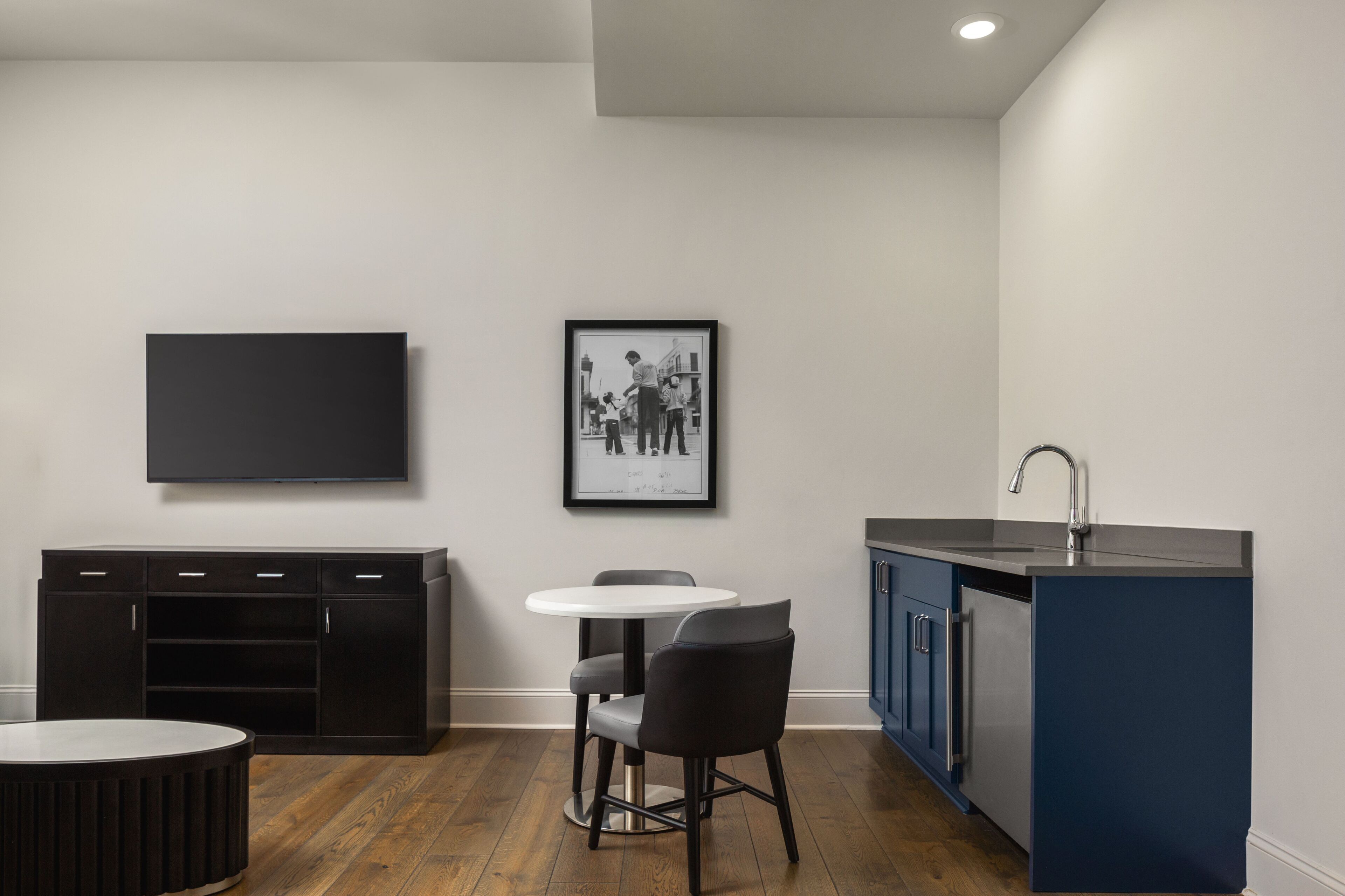 A modern kitchen with a dining area, a flat-screen TV, and a framed picture on the wall.