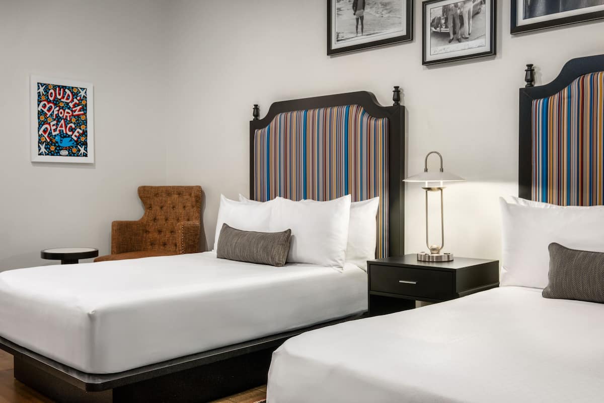 Ein Hotelzimmer mit zwei Betten, einem braunen Sessel, einem kleinen Tisch und einer Lampe.