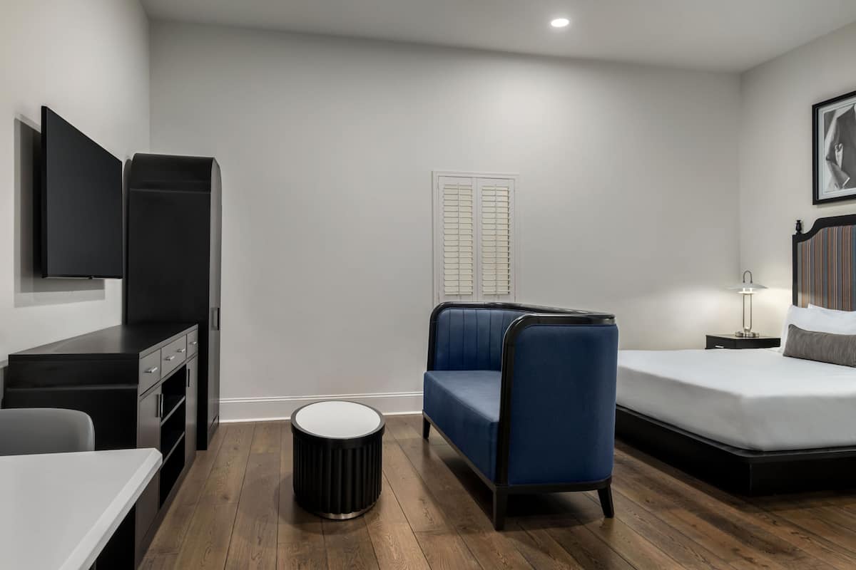 Ein modernes Hotelzimmer mit einem Bett, einer Couch, einem Schreibtisch, einem Fernseher und einem Fenster mit Rollläden.